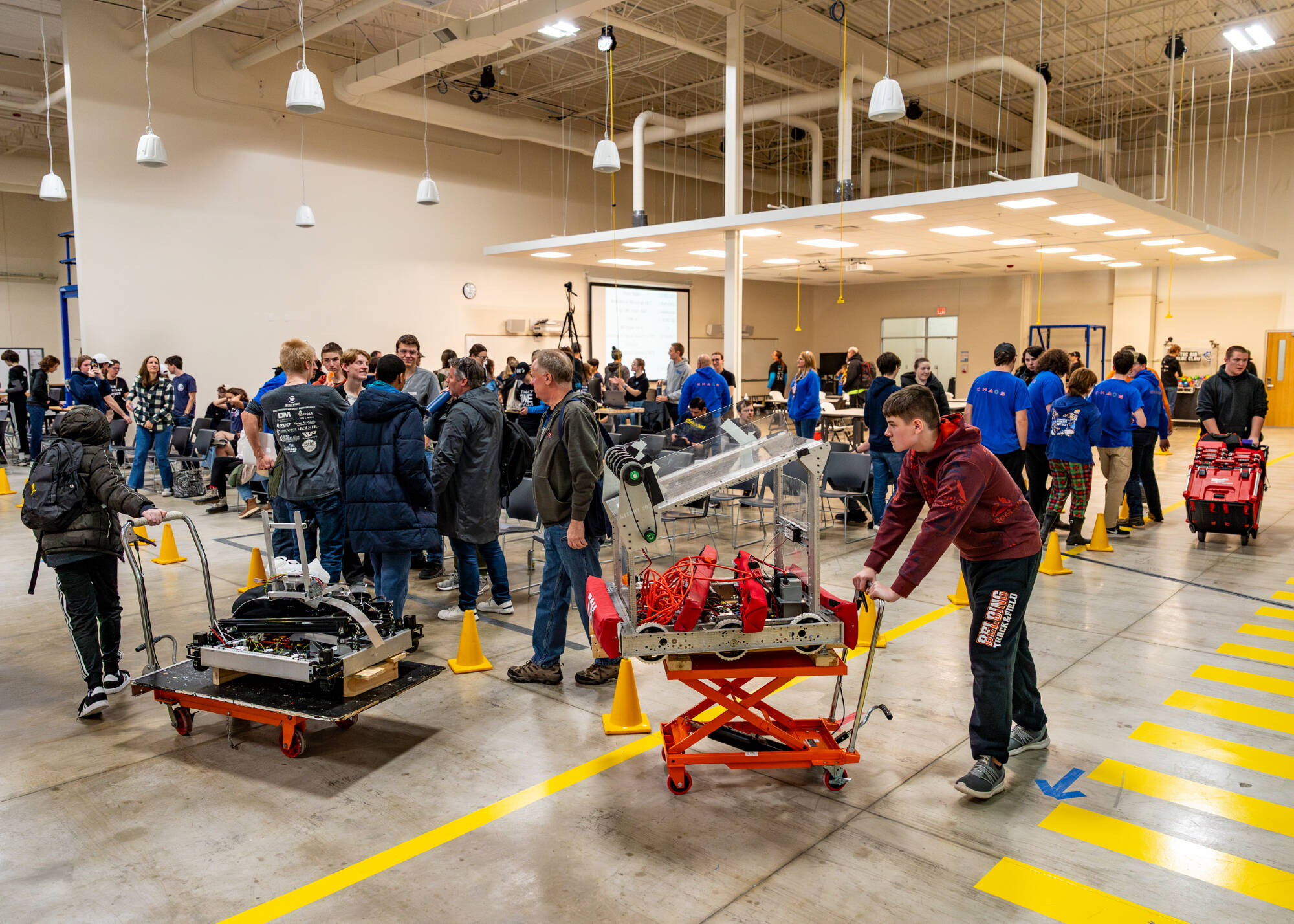 Students pack up and transport robots on wheeled carts inside GVSU's IDC robotics practice field.